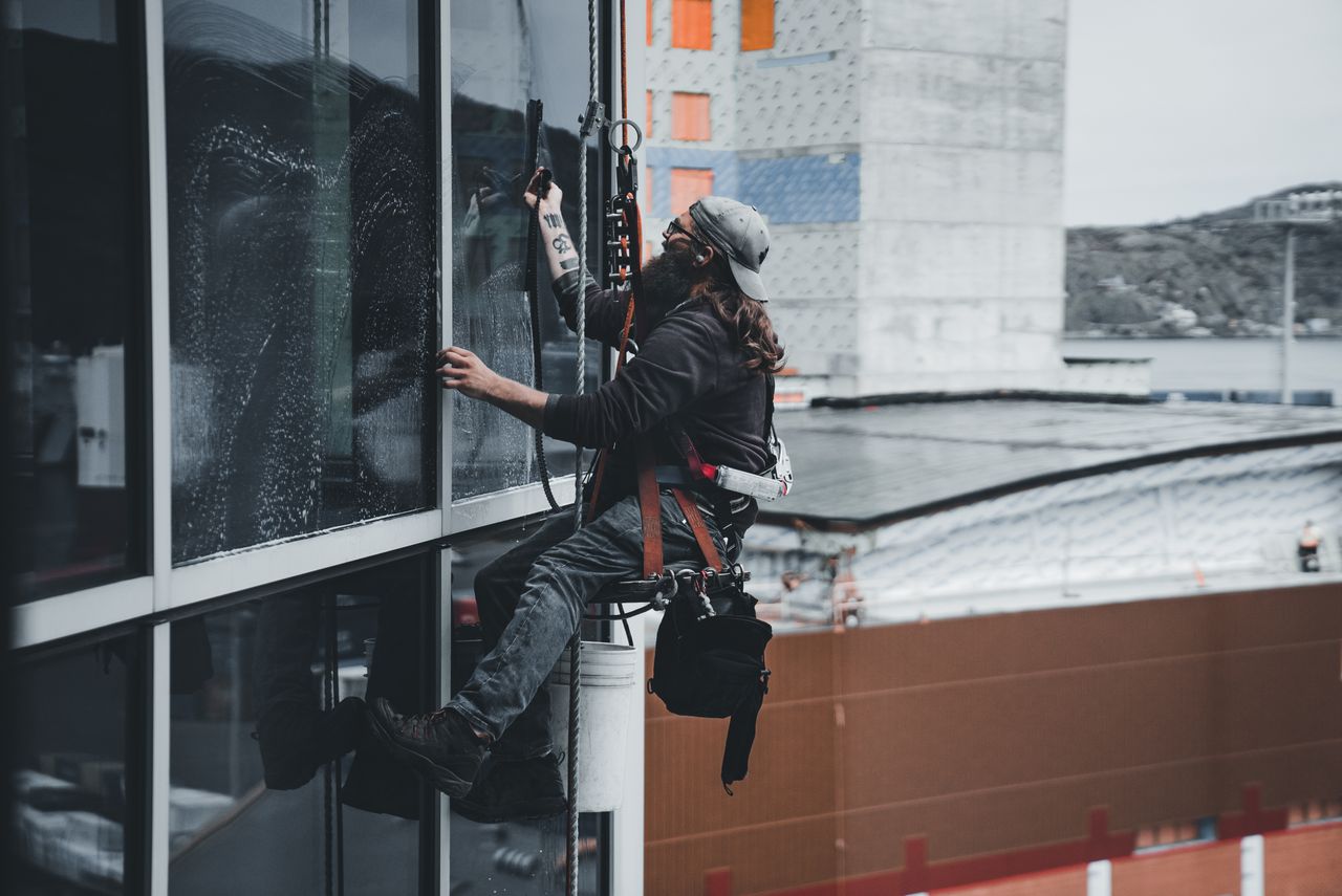 services-01 A man cleaning skyscraper windows with a harness, highlighting urban high-rise maintenance work.